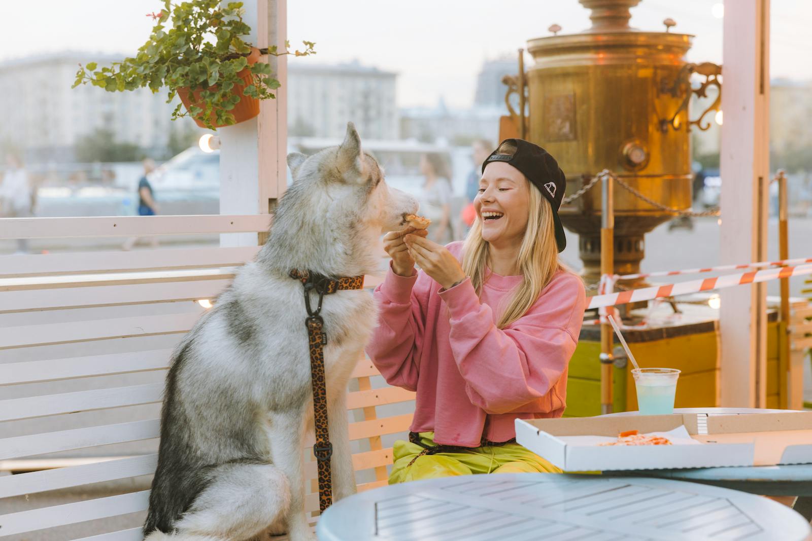 A joyful moment of a woman sharing pizza with her husky dog at an outdoor café.
