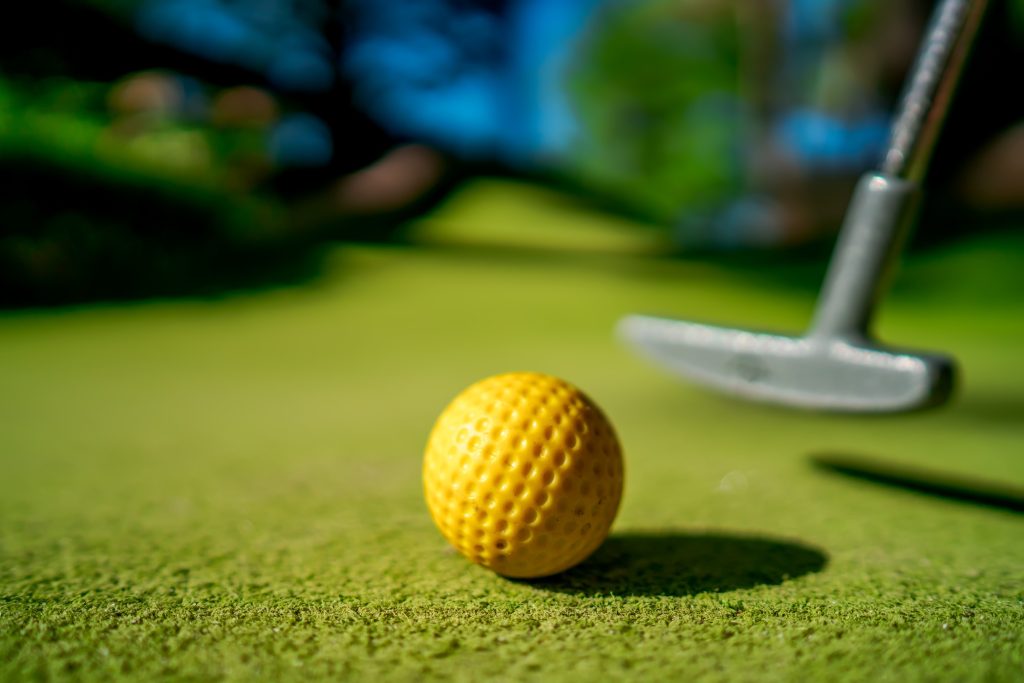 mini-golf-yellow-ball-with-a-bat-near-the-hole-at-sunset.jpg