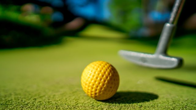 mini-golf-yellow-ball-with-a-bat-near-the-hole-at-sunset.jpg